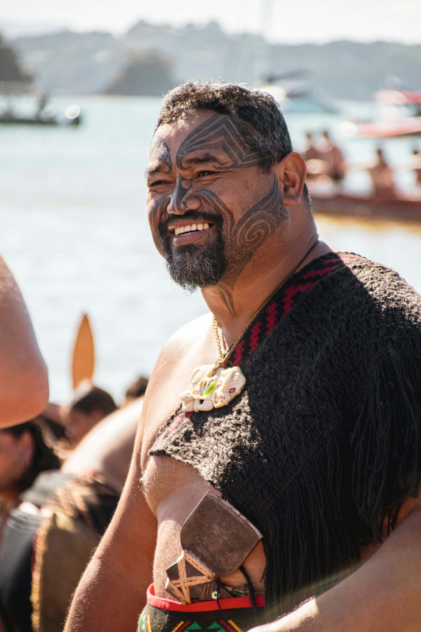 A Māori community member in traditional dress smiling warmly at a cultural gathering